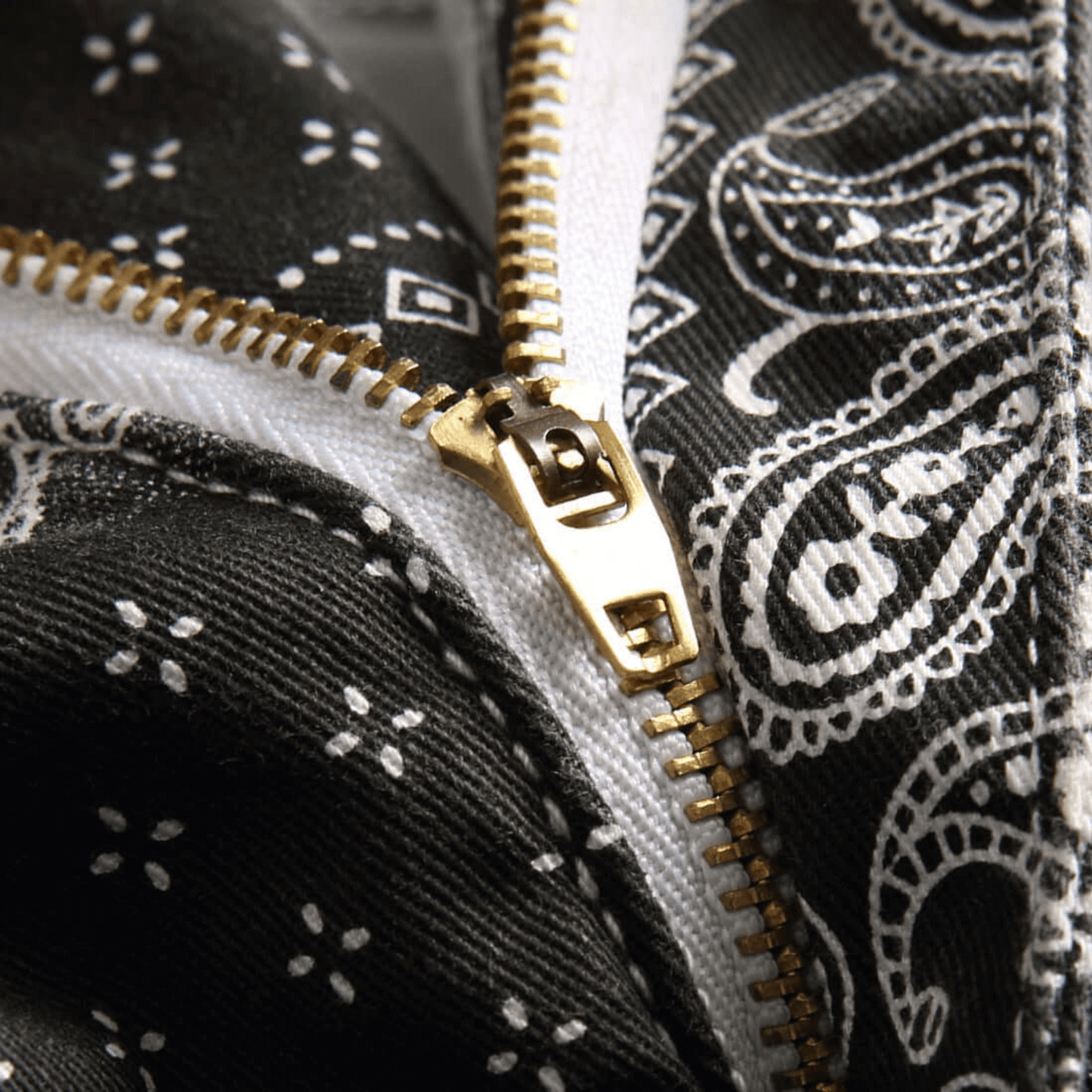 Close-up of a zippered detail on a black paisley print denim fabric, showcasing premium quality and retro style.