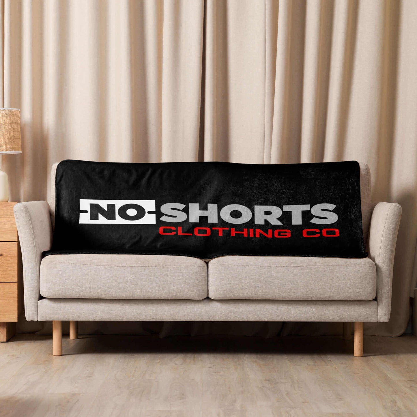 NO SHORTS CO. Sherpa blanket displayed on a couch, showcasing its soft texture and stylish logo design.