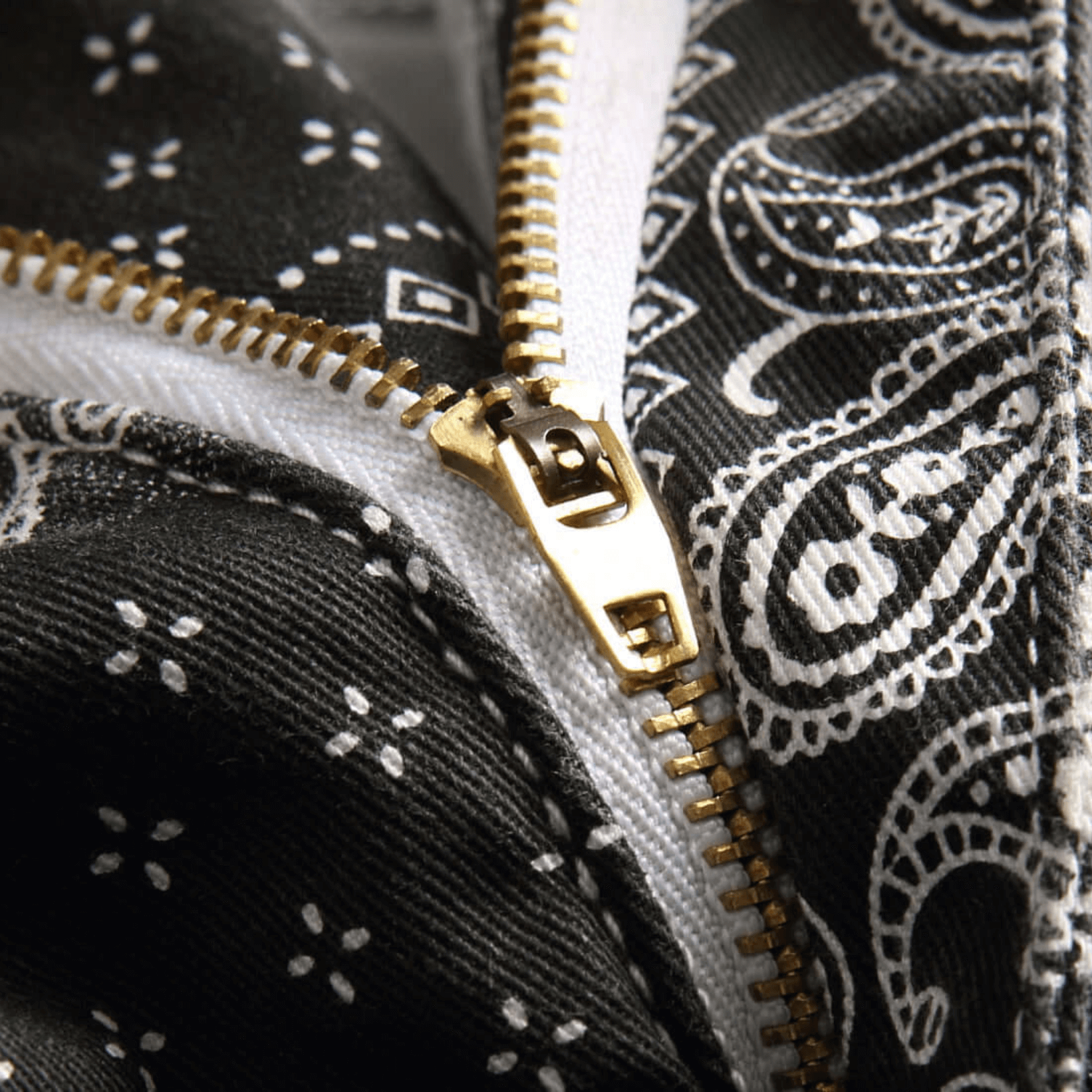 Close-up of a zippered detail on a black paisley print denim fabric, showcasing premium quality and retro style.